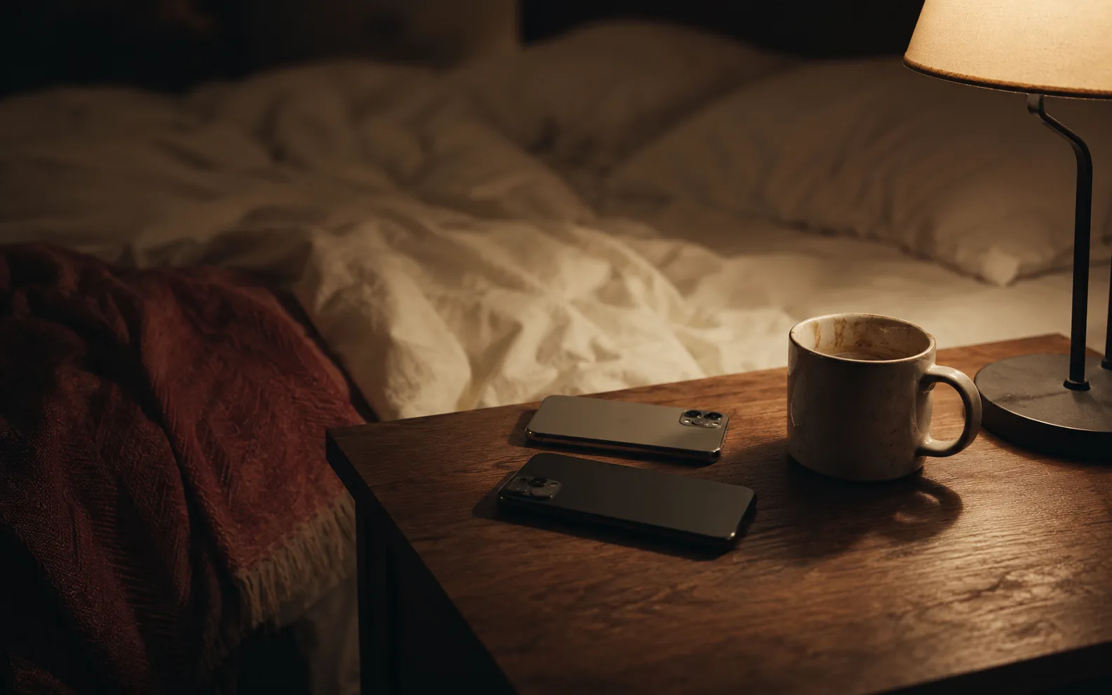 夜のベッドサイド、二つのスマホと使い古したマグカップ、暖かい間接照明